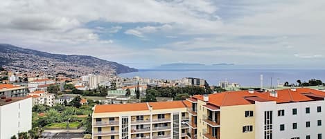 A coastal cityscape with a prominent apartment building featuring balconies and a view of the sea.