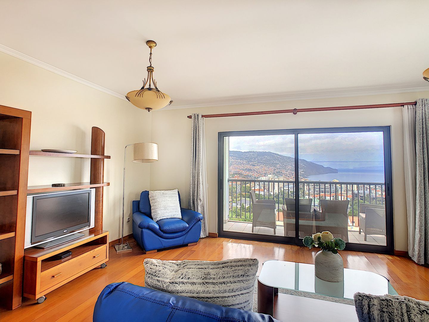 Ein Wohnzimmer mit Fernseher, blauem Sofa und Balkon mit Blick auf die Stadt.