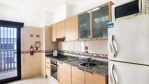 A kitchen with wooden cabinets, a stainless steel sink, a microwave, and a refrigerator. - Gemini Apartment by LovelyStay (Funchal)