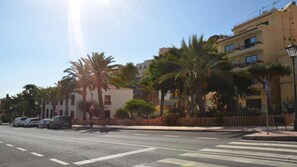 A street with palm trees, a pedestrian crossing, and buildings with balconies.
