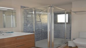 Een badkamer met een douchecabine van glas, een witte wastafel met spiegel en een toilet.