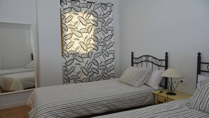 Une chambre à coucher comprenant un lit, une table de chevet, une lampe, un miroir et un mur orné d’un motif de feuilles.