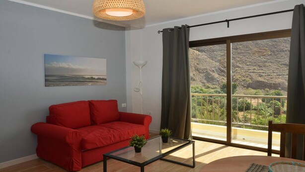 Un salon avec un canapé rouge, une table basse en verre, un lampadaire et une grande fenêtre donnant sur un paysage montagneux.