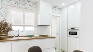 A modern kitchen with white cabinets, a wooden countertop, a built-in oven, and a glass dining table. - Genteel Home Juan Rabadan I (Seville)
