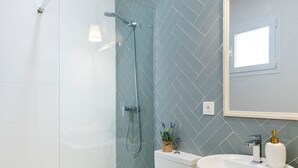 A modern bathroom with a glass-enclosed shower, a white sink, and a wooden vanity. - Genteel Home Juan Rabadan I (Seville)