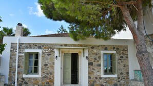 A stone building with a central door and two windows with shutters, surrounded by trees. - Stone House Kleio Kos  (Αντιμάχεια)