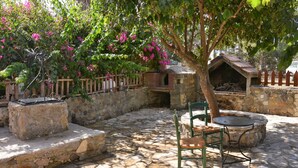 A stone patio with a brick oven, a wooden fence, and a tree with pink flowers. - Stone House Kleio Kos  (Αντιμάχεια)