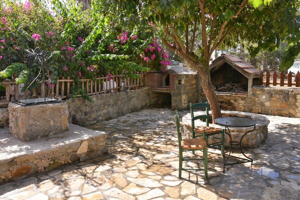 Un patio de piedra con un horno de ladrillo, una valla de madera y un árbol de flores rosadas.