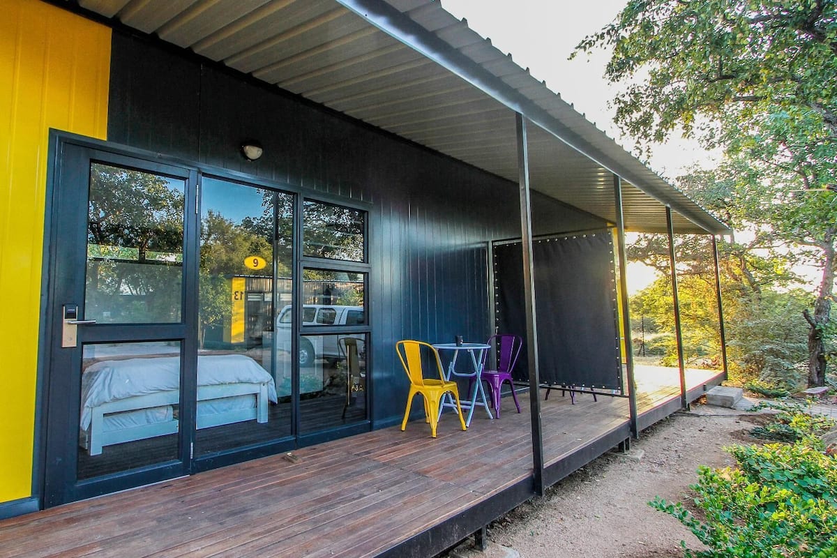 A modern building with a wooden deck, large glass windows, and colorful chairs.