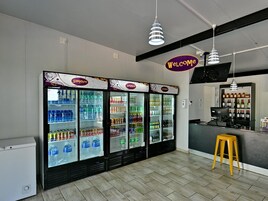 Interior limpo e moderno, com uma placa de 'Welcome', área de bar e vários dispensadores de bebidas.