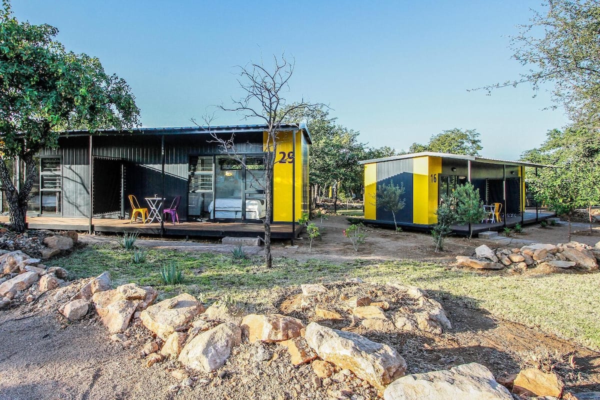 Two yellow and black cabins with outdoor seating, surrounded by rocks and sparse vegetation.