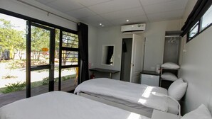 A hotel room with two beds, a small desk, a mirror, and an air conditioning unit. - SleepOver Beitbridge (Musina)