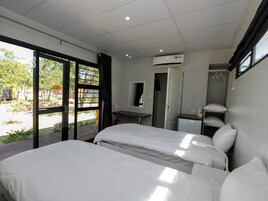 Quarto de hotel com duas camas, uma secretária pequena, um espelho e um aparelho de ar condicionado.