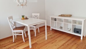 A room with a white table and chairs, a wooden floor, and a white cabinet with shelves. - Modern city apartment with balcony and private parking space in a quiet location (Kiel)