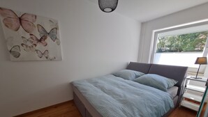 A bedroom with a bed, a window, a wall-mounted artwork of butterflies, and a bedside lamp. - Modern city apartment with balcony and private parking space in a quiet location (Kiel)