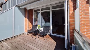 A balcony with a wooden deck, two black chairs, a small table, and a potted sunflower. - Modern city apartment with balcony and private parking space in a quiet location (Kiel)