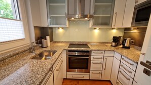 A modern kitchen with granite countertops, stainless steel appliances, and white cabinetry. - Modern city apartment with balcony and private parking space in a quiet location (Kiel)