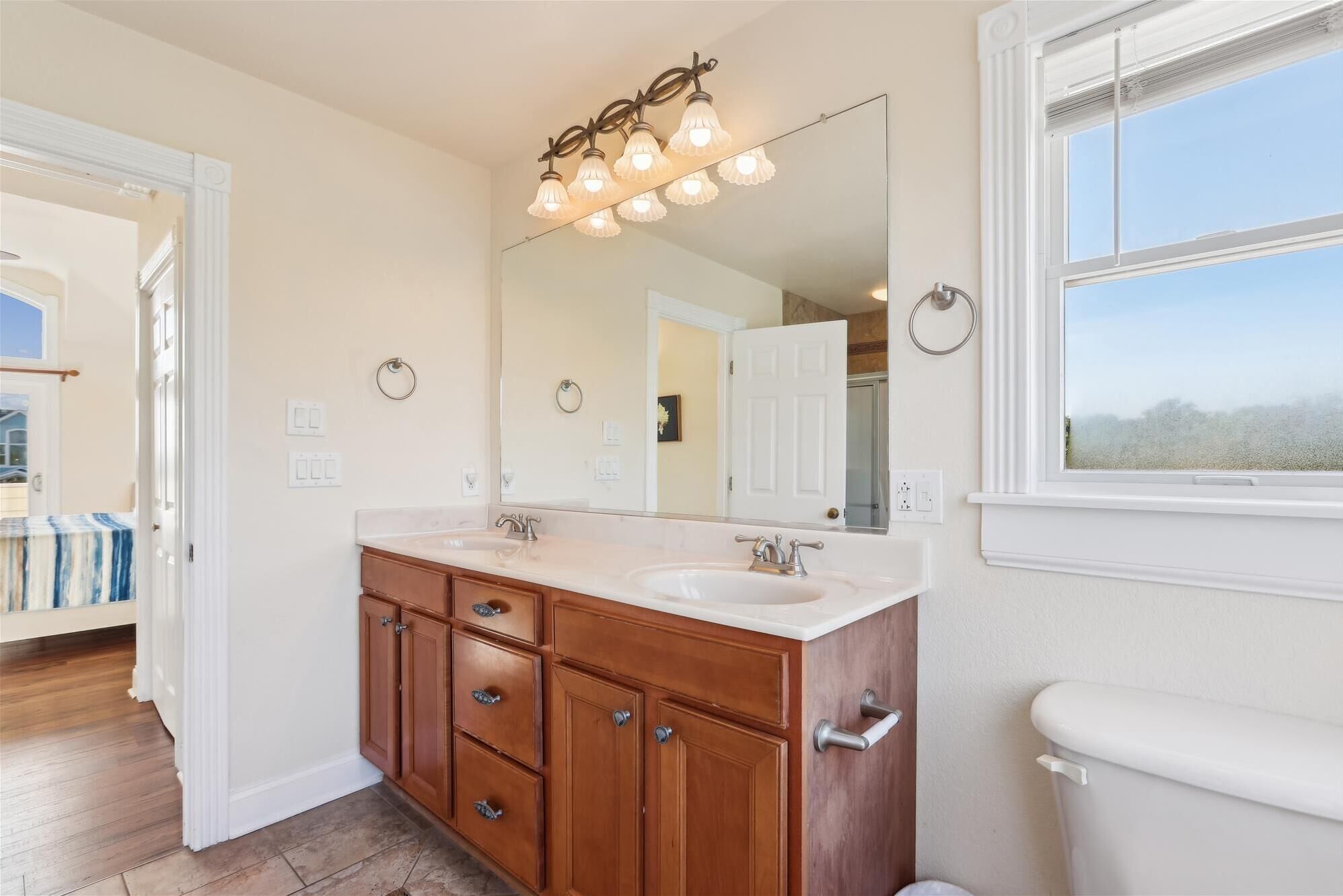 A bathroom with a double sink vanity, wooden cabinets, a large mirror, and a window with a view.