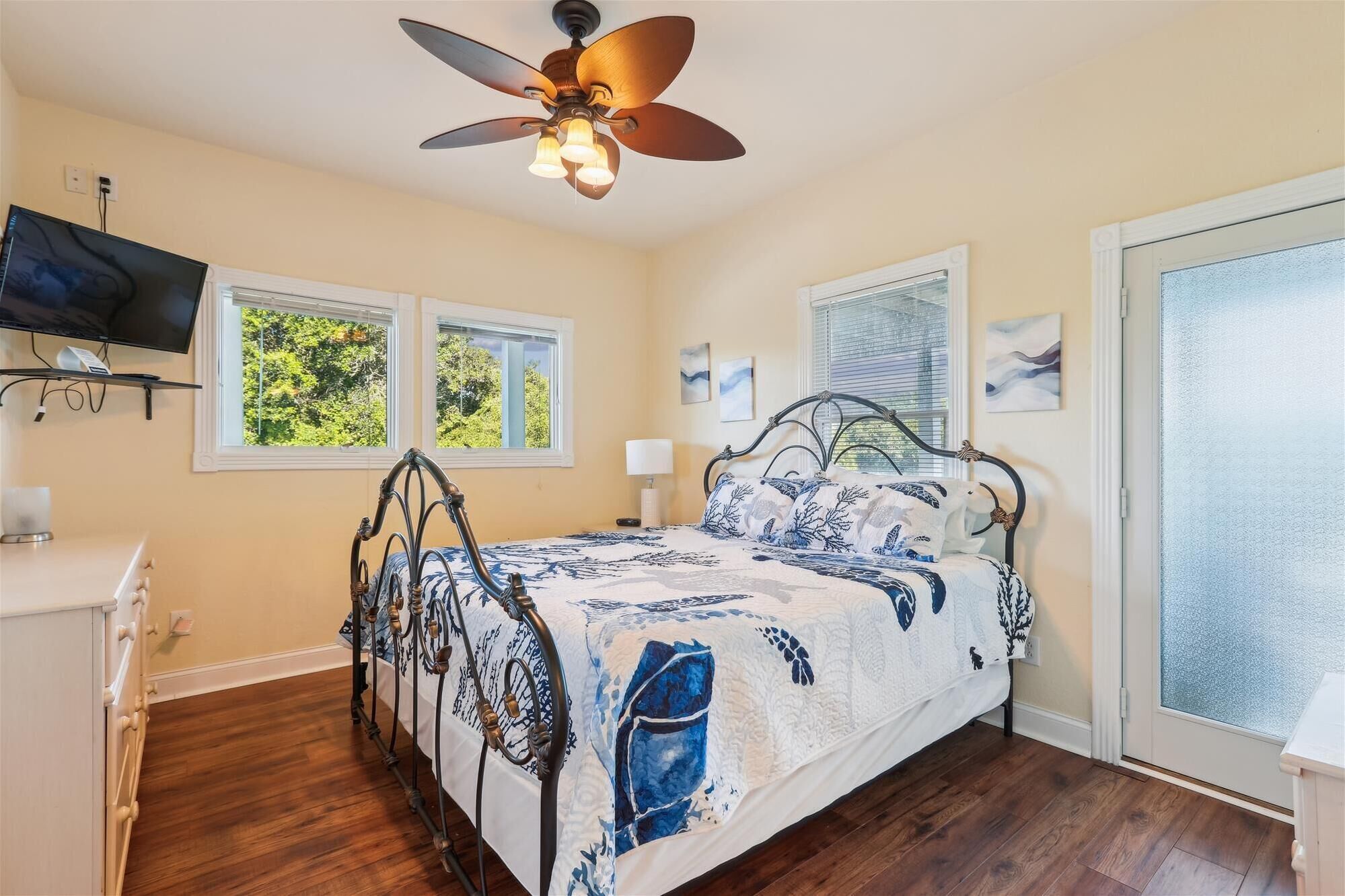 A bedroom with a bed, a ceiling fan, a TV, and two windows.