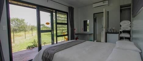 A bedroom with a large bed, a wardrobe, a desk, and a view of the outdoors.