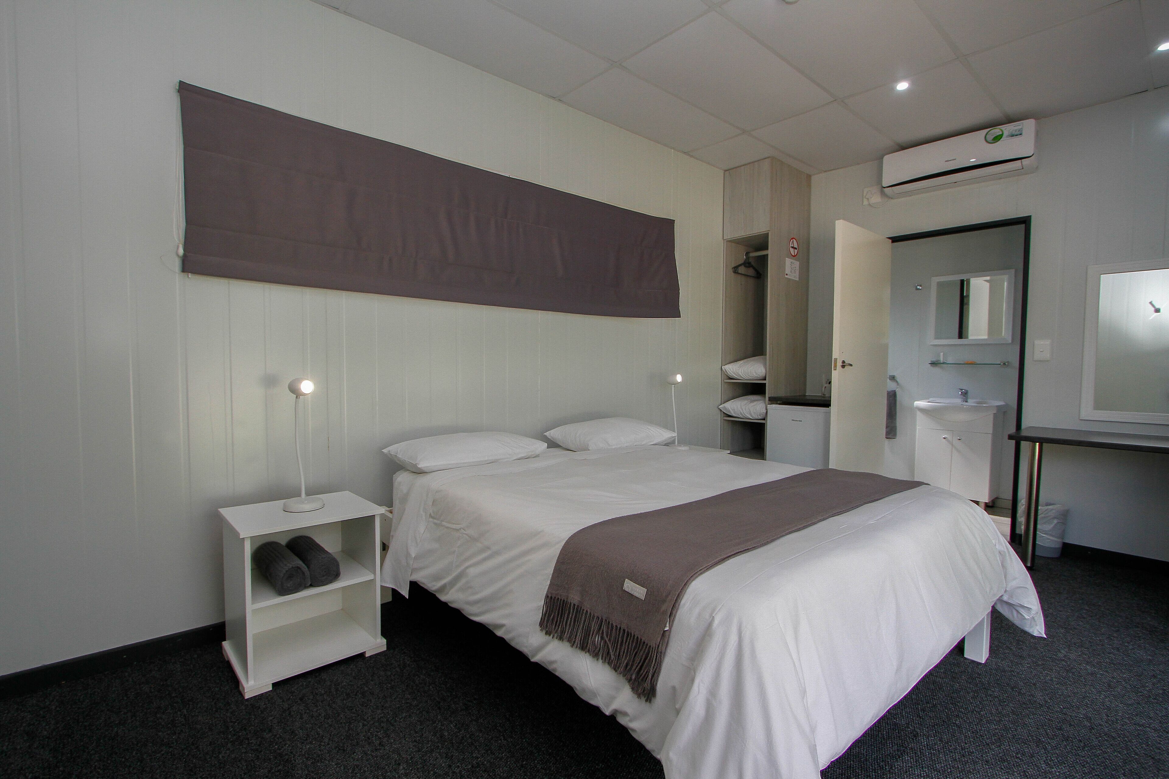 Et hotelværelse med seng, et natbord med lampe, et klædeskab, et spejl og en aircondition.