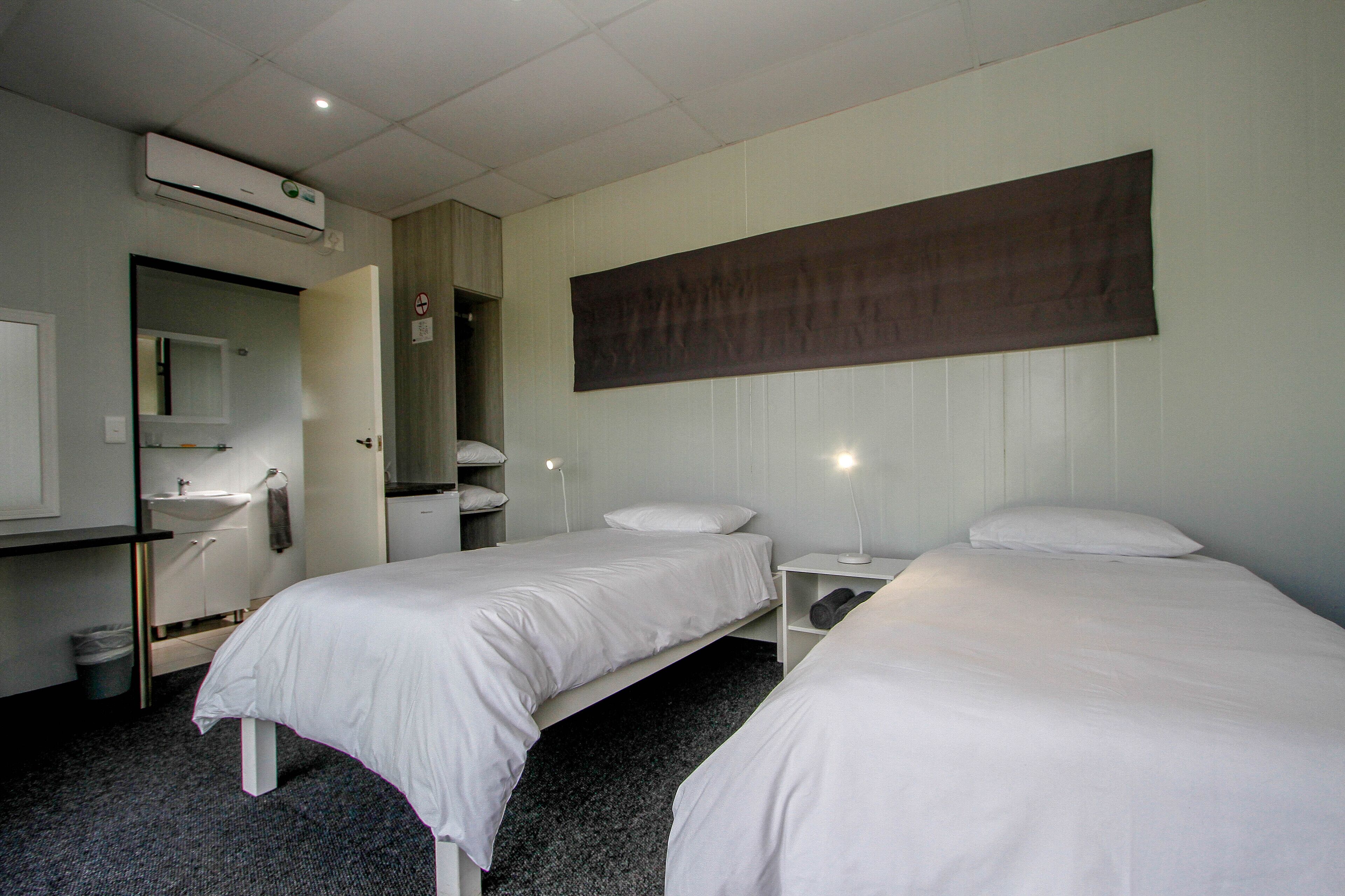 A hotel room with two single beds, a large mirror, a sink, and a wall-mounted air conditioner.
