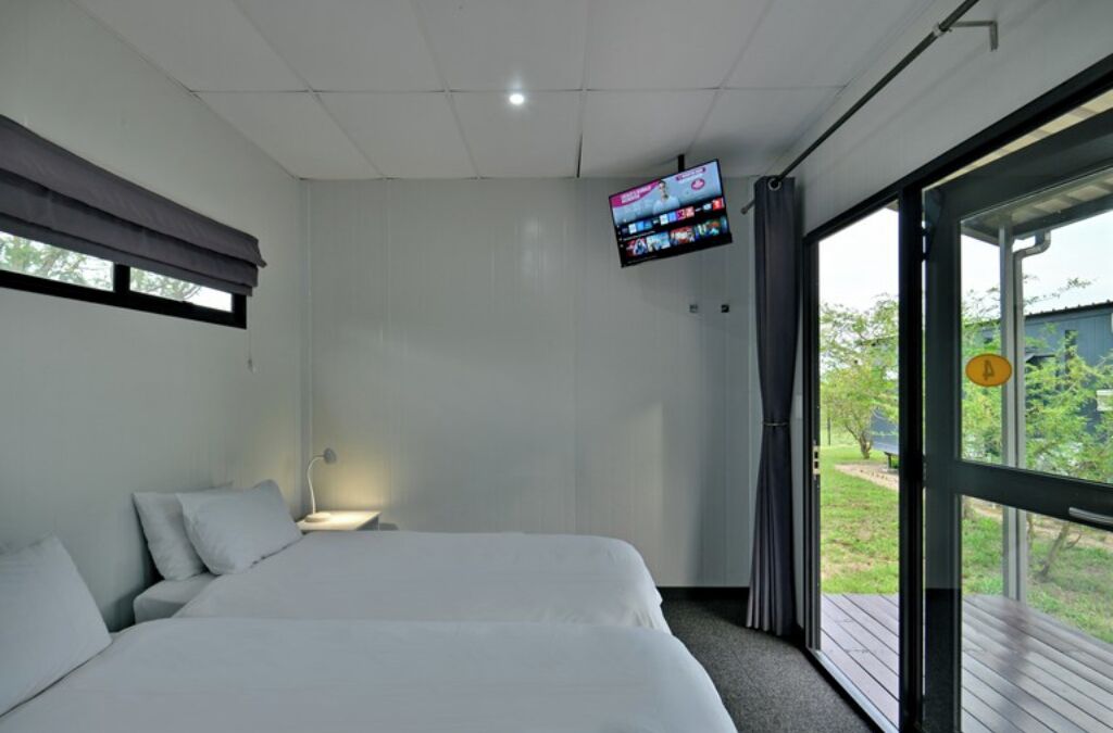 A bedroom with a bed, a TV mounted on the wall, and a window with a view of greenery.