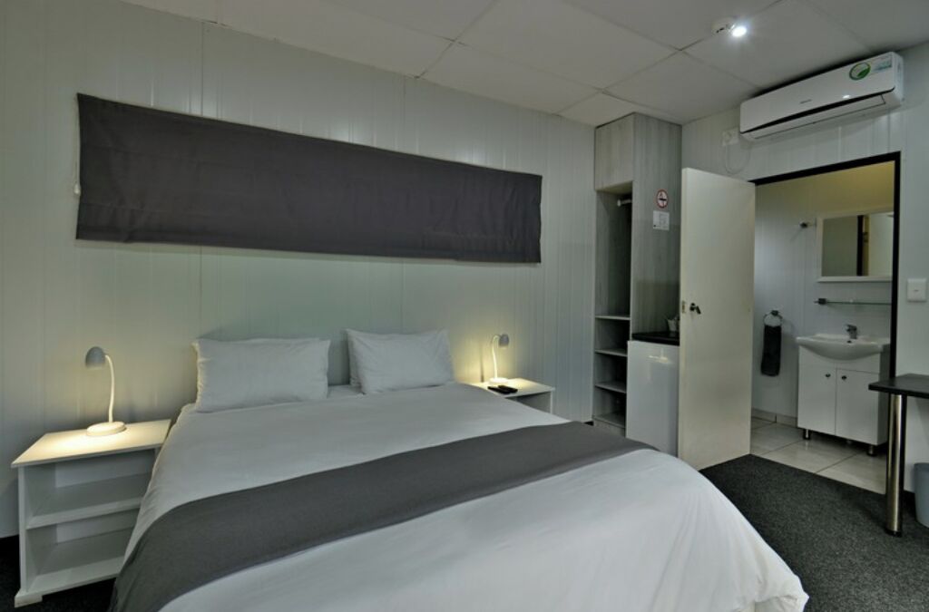 A hotel room with a bed, bedside tables, a wardrobe, a mirror, and a bathroom with a sink and toilet.
