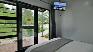 Un dormitori amb un llit, una televisió penjada a la paret i una porta corredissa de vidre que dona a una zona exterior.
