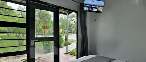 A bedroom with a bed, a television mounted on the wall, and a sliding glass door leading to an outdoor area.