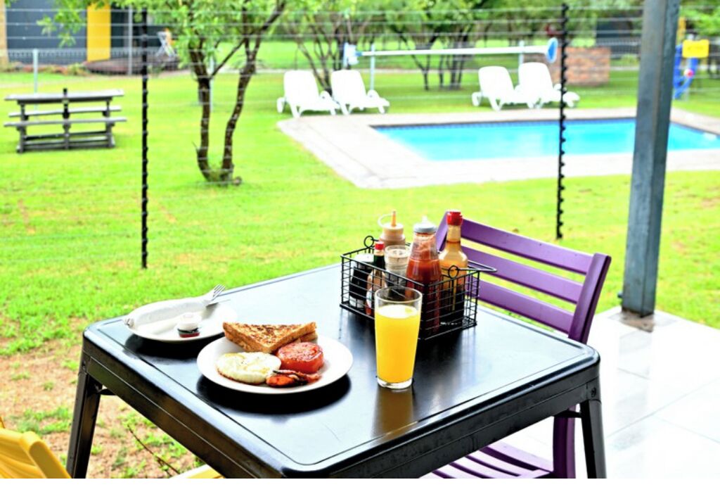 A table with breakfast items and a glass of orange juice, a purple chair, and a view of a swimming pool and lawn chairs.