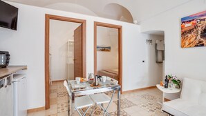 A compact living space with a dining table, chairs, a sofa, a TV, and a kitchen area. - Tiny House 21 Bright Aparment (Polignano a Mare)