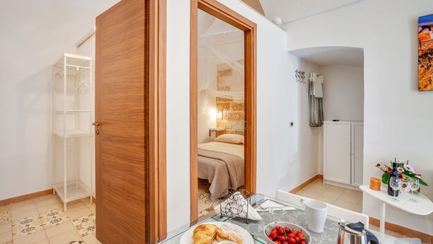 A compact room with a bed, a small table with breakfast items, a white wardrobe, and a view of a bedroom through an open door. - Tiny House 21 Bright Aparment (Polignano a Mare)