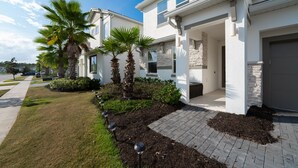 A modern two-story house with a paved driveway, palm trees, and a well-maintained lawn.