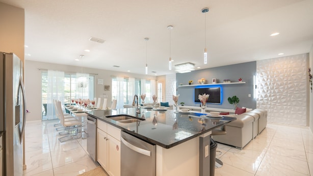 A modern kitchen with a central island, stainless steel appliances, and a dining area with white chairs.