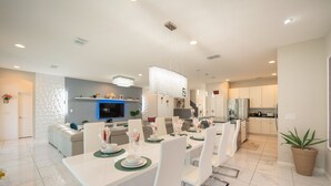 A modern dining area with a white table set for six, surrounded by white chairs.