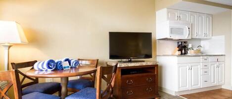 A compact hotel room with a dining table, chairs, a television, a microwave, and a kitchenette.