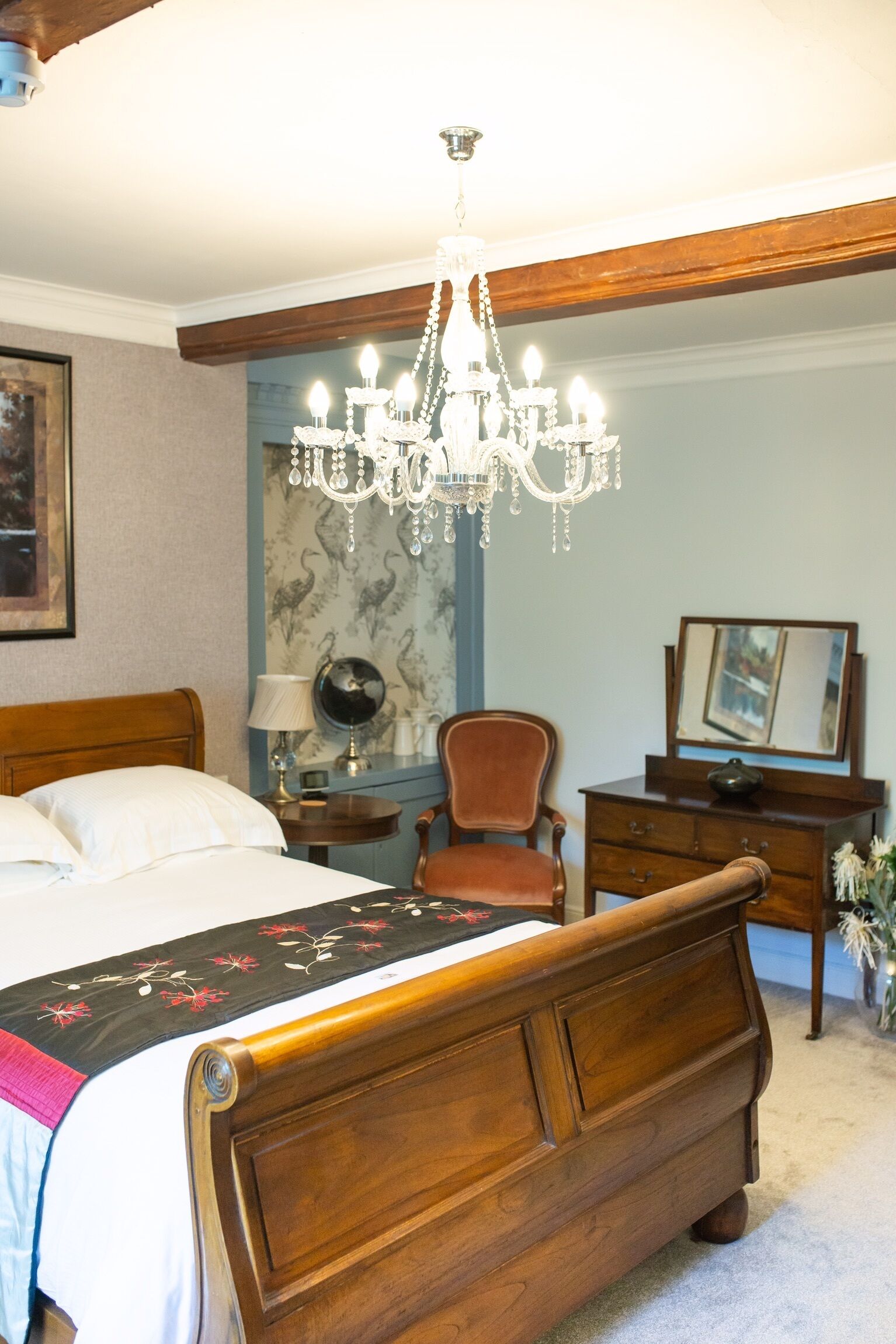 Quarto com cama de madeira, lustre, cadeira, cômoda e espelho.