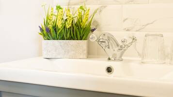 Une salle de bain avec un pare-baignoire en marbre, un lavabo blanc, un vase en verre avec des fleurs et une carafe en verre.