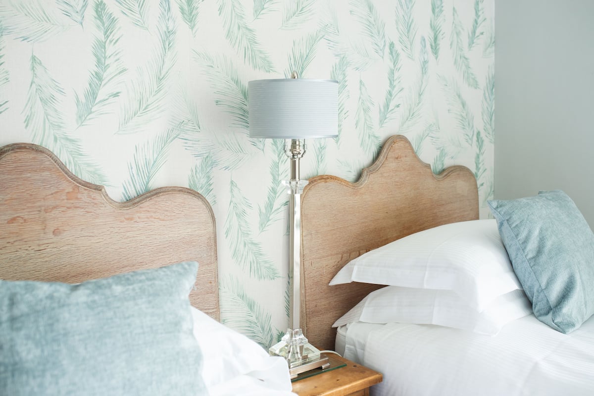 A neatly made bed with white linens, a wooden headboard, and a nightstand with a lamp and a glass object.