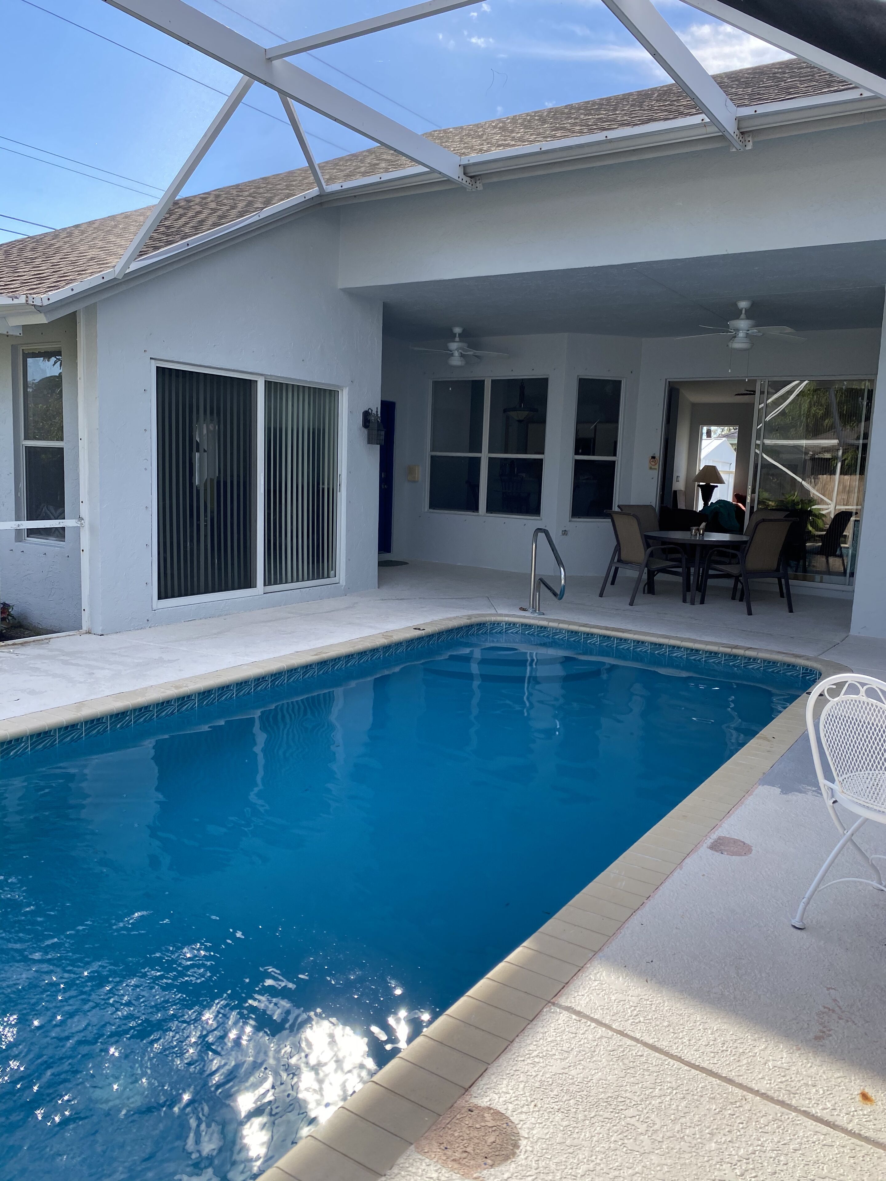 A swimming pool with a clear blue water, surrounded by a covered patio area with a table and chairs.
