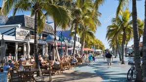 Een strandcafé met terras, palmbomen en een helderblauwe lucht.