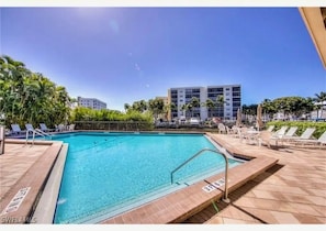 Une piscine avec une terrasse carrelée, des chaises longues et un ciel d’un bleu limpide.
