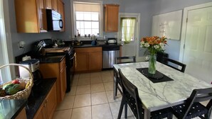 A kitchen with wooden cabinets, a marble countertop, a dining table with chairs, and a vase of flowers. - Spacious Egleston Sq 3 Bedroom, Dog Friendly (Boston)