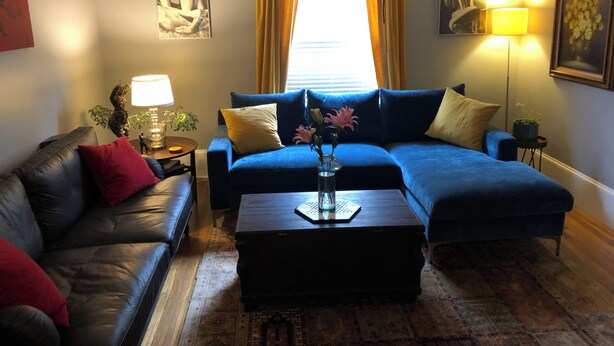 A living room with a blue sofa, a black leather couch, a coffee table, and a patterned rug. - Spacious Egleston Sq 3 Bedroom, Dog Friendly (Boston)