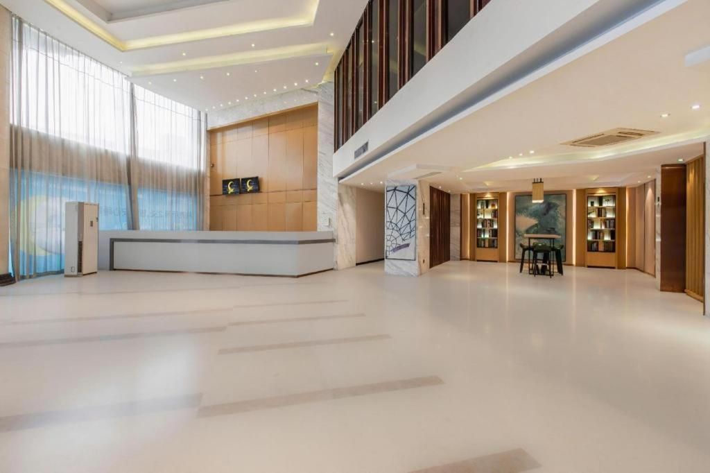 A spacious lobby with a reception desk, a seating area, and a large window with curtains.