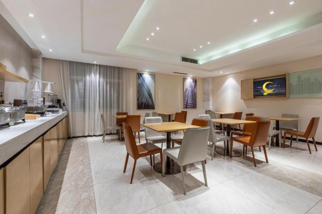 A modern hotel dining area with multiple tables and chairs, a counter with a coffee machine, and a large window with curtains.