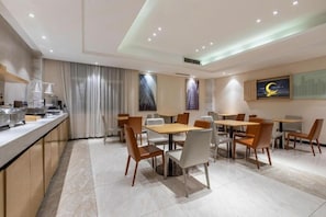 A modern hotel dining area with multiple tables and chairs, a counter with a coffee machine, and a large window with curtains. - City Comfort Inn Wuhan Fengshu Er Road Baijin Mansion (Wuhan)