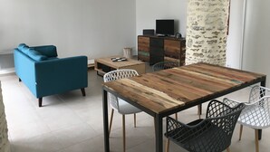 A modern living room with a blue sofa, a wooden dining table with chairs, and a TV on a wooden cabinet. - Maison Charme 70m2 Saint Georges Oléron (Saint-Georges-d'Oléron)