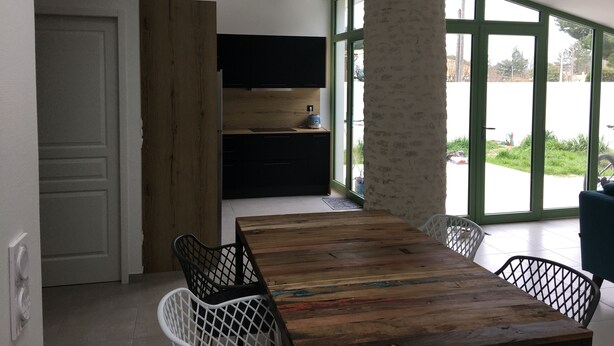A modern kitchen with wooden cabinets, a built-in TV, and a large window offering a view of the outdoors. - Maison Charme 70m2 Saint Georges Oléron (Saint-Georges-d'Oléron)